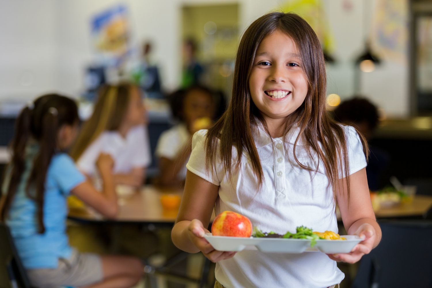 Smiling girl in school cafeteria holding lunch tray.
